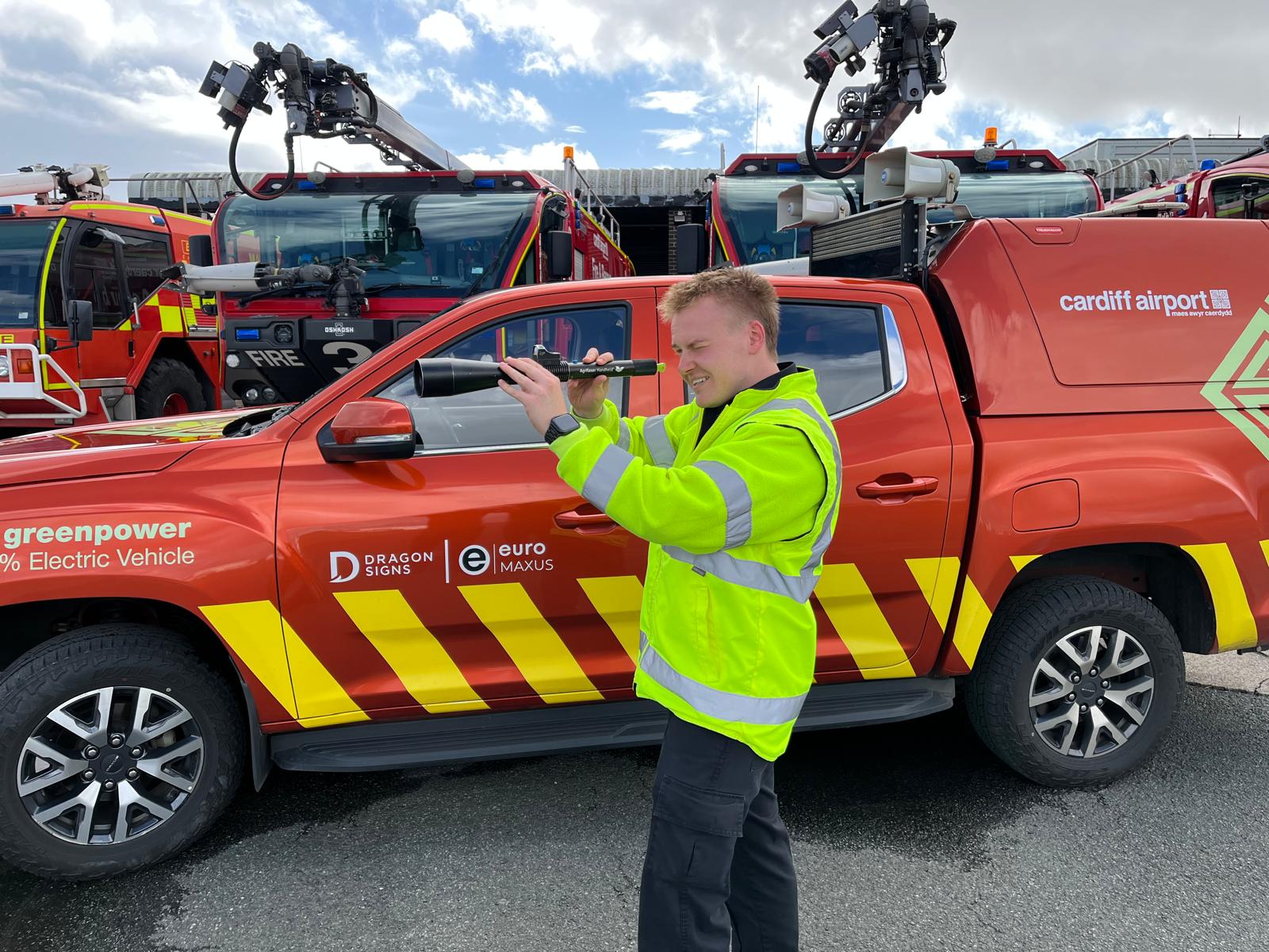 Airfield Operations Technician at Cardiff Airport demonstrating AVIX Handheld Laser Bird Deterrent in front of emergency response vehicles on the airfield