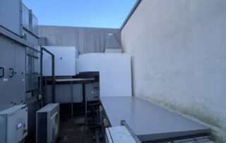 Open service area with ventilation equipment units and ducting, with bird netting installed overhead between the surrounding walls.